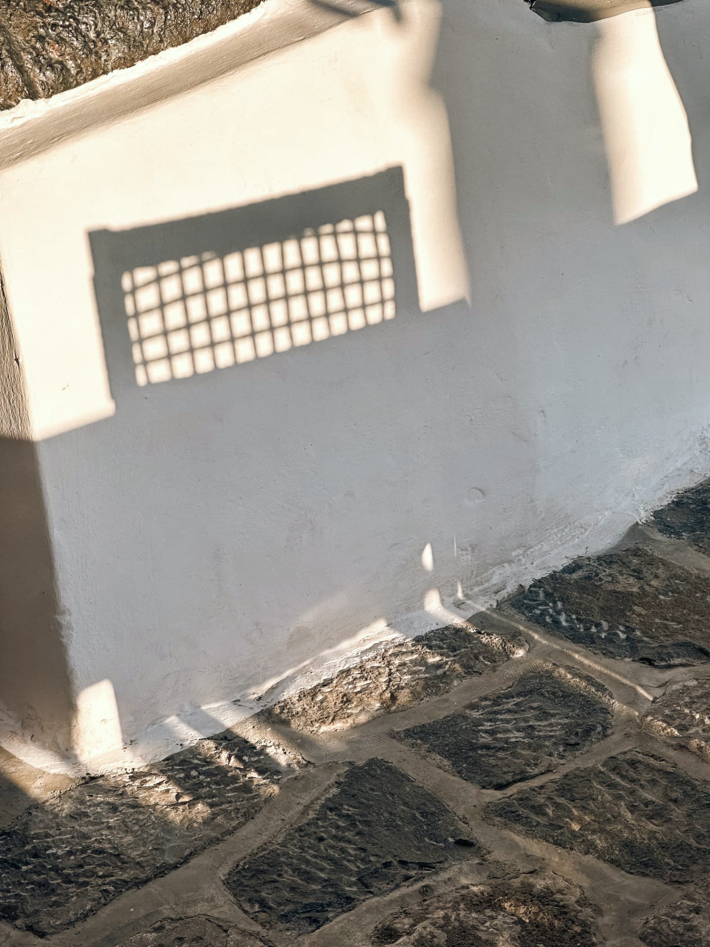 Window grille shadow cast across a whitewashed Hydra wall