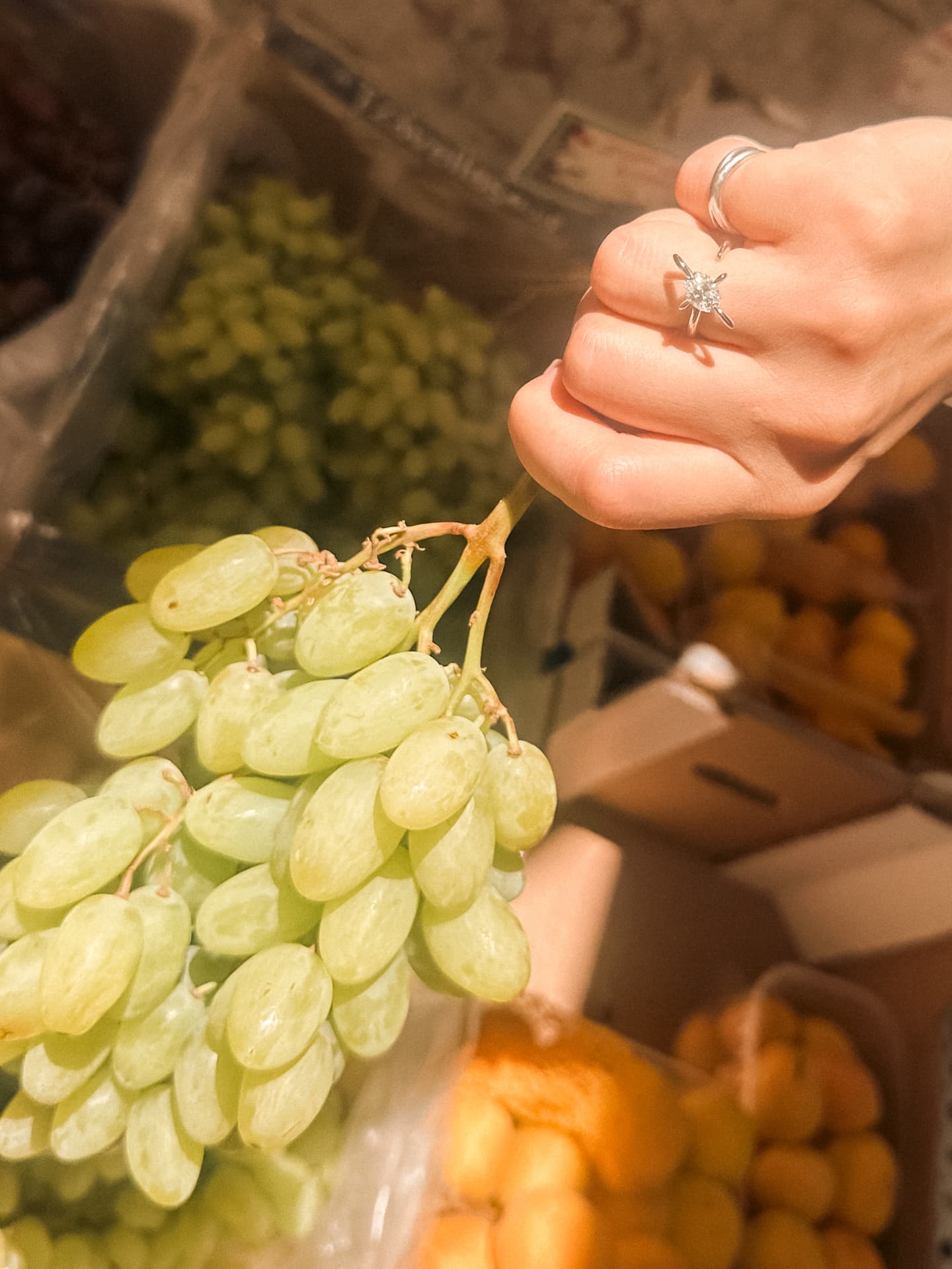 Hand wearing a Solera diamond ring picking grapes at the market